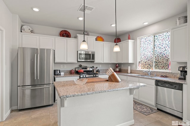 kitchen with white cabinetry, appliances with stainless steel finishes, decorative light fixtures, light stone counters, and a center island