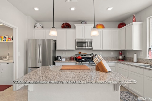 kitchen featuring hanging light fixtures, washer and clothes dryer, appliances with stainless steel finishes, and white cabinetry