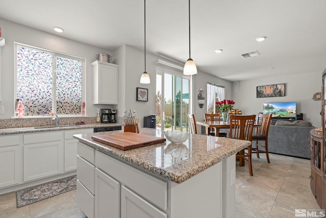 kitchen with white cabinets, a center island, decorative light fixtures, sink, and light stone counters