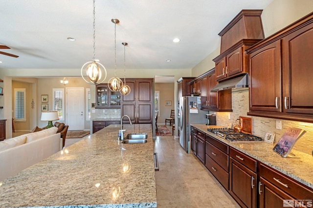 kitchen featuring stainless steel appliances, sink, pendant lighting, backsplash, and ceiling fan with notable chandelier