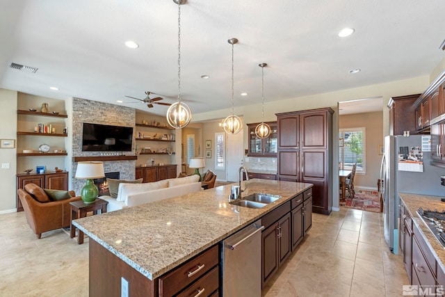 kitchen featuring sink, dishwasher, a stone fireplace, and a center island with sink