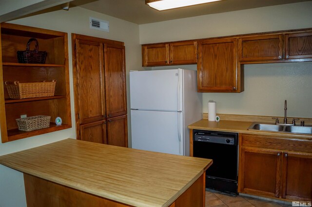 kitchen with light tile patterned flooring, black dishwasher, sink, and white fridge