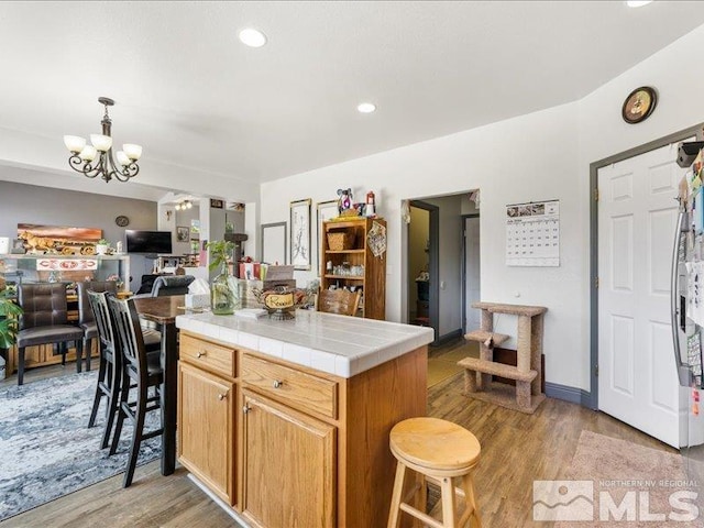 kitchen with light wood-style flooring, a kitchen island, tile counters, a kitchen bar, and an inviting chandelier