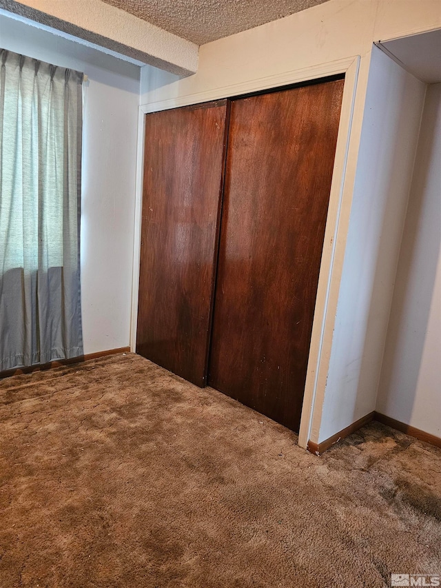 unfurnished bedroom featuring carpet floors, a textured ceiling, and a closet