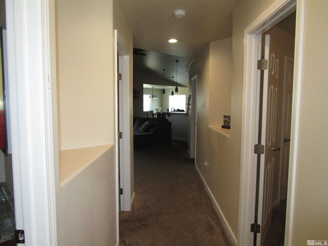 hall with dark carpet and lofted ceiling