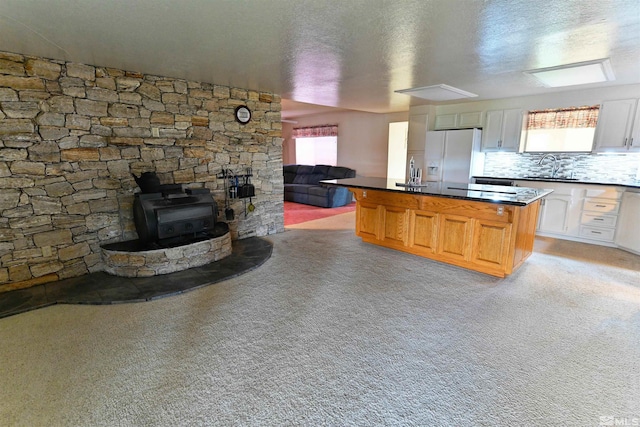 kitchen with light carpet, backsplash, a kitchen island, a wood stove, and white refrigerator with ice dispenser