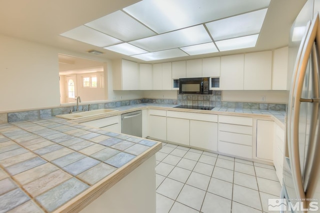 kitchen with tile countertops, black appliances, sink, light tile patterned flooring, and white cabinets