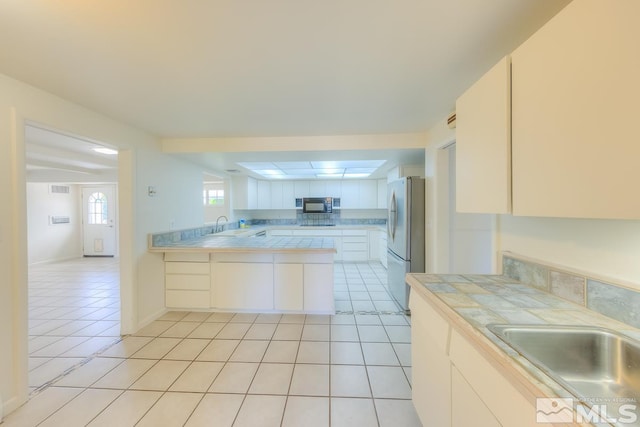 kitchen with white cabinetry, kitchen peninsula, stainless steel fridge, and tile counters