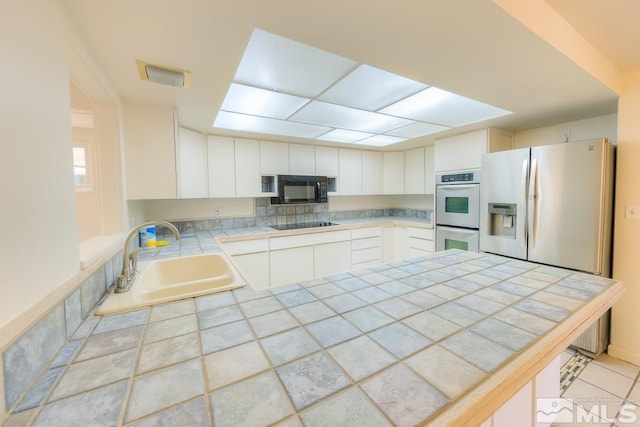 kitchen featuring tasteful backsplash, black appliances, sink, tile counters, and white cabinets