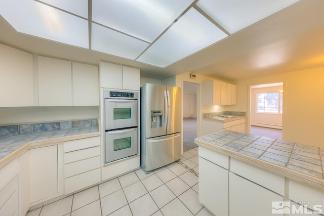 kitchen featuring a baseboard heating unit, light tile patterned floors, appliances with stainless steel finishes, tile counters, and white cabinets