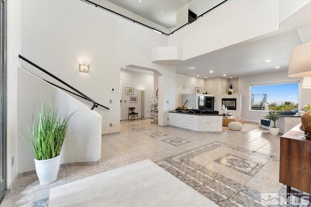 living room featuring arched walkways, a fireplace, a towering ceiling, and baseboards