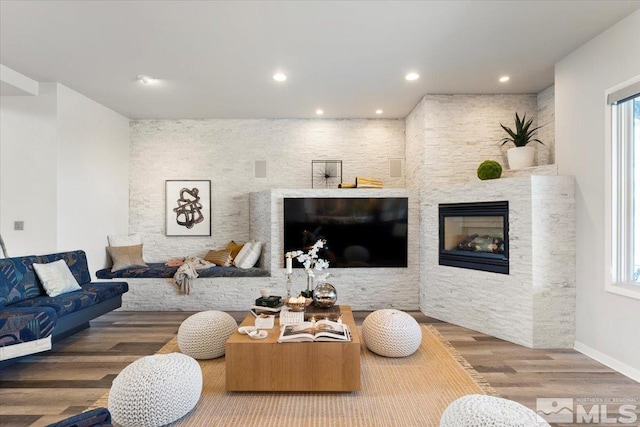 living room featuring a glass covered fireplace, baseboards, recessed lighting, and wood finished floors