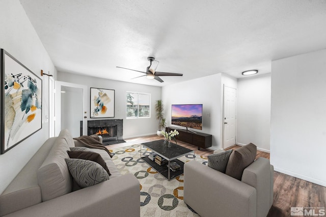 living room featuring wood-type flooring, a tiled fireplace, a textured ceiling, and ceiling fan