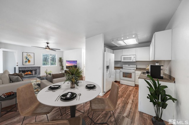 dining room with ceiling fan, a tile fireplace, and dark wood-type flooring