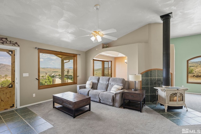 living room featuring a wood stove, vaulted ceiling, dark tile patterned flooring, and ceiling fan