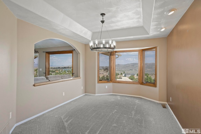 unfurnished room with a chandelier, a healthy amount of sunlight, carpet floors, and a tray ceiling