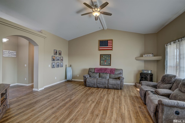 living room with ceiling fan, light hardwood / wood-style flooring, lofted ceiling with beams, and a wood stove