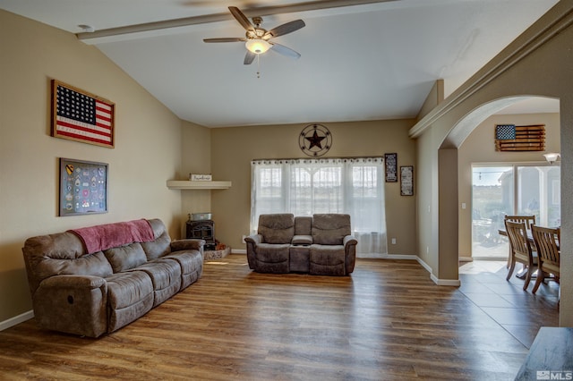 living room featuring wood-type flooring, ceiling fan, a wood stove, and vaulted ceiling with beams