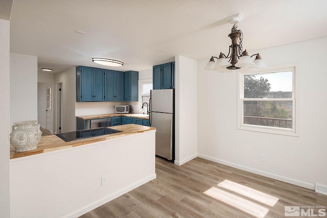 kitchen with pendant lighting, blue cabinetry, stainless steel appliances, kitchen peninsula, and light wood-type flooring