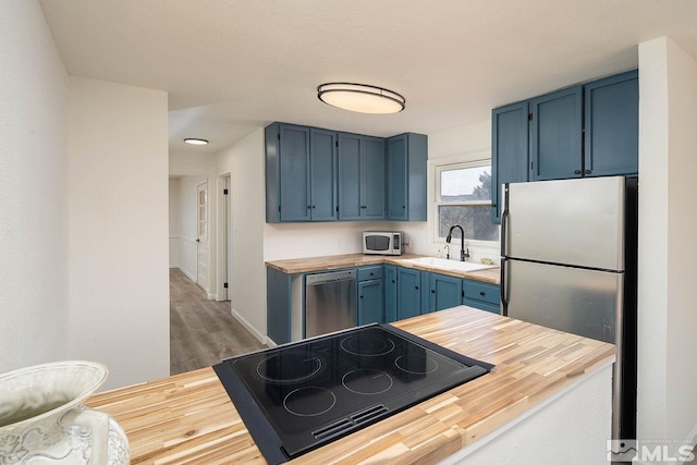 kitchen featuring blue cabinets, appliances with stainless steel finishes, sink, and hardwood / wood-style floors