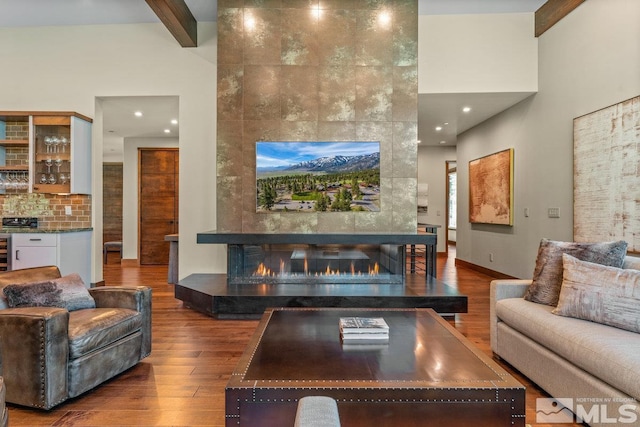 living room featuring a tiled fireplace, indoor bar, hardwood / wood-style floors, and beam ceiling