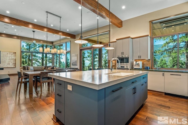 kitchen with white cabinetry, a kitchen island with sink, sink, and decorative light fixtures