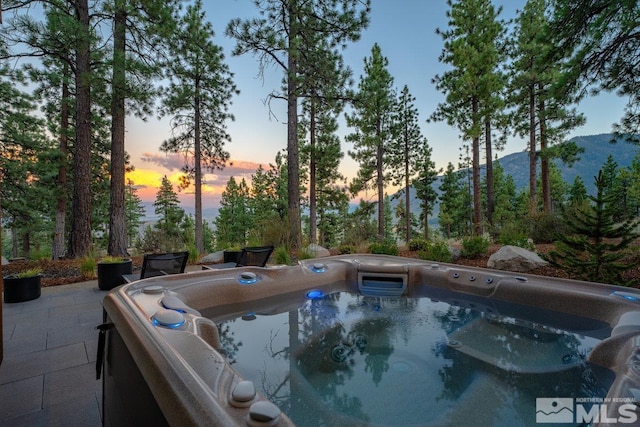 pool at dusk featuring a hot tub, a patio, and a mountain view