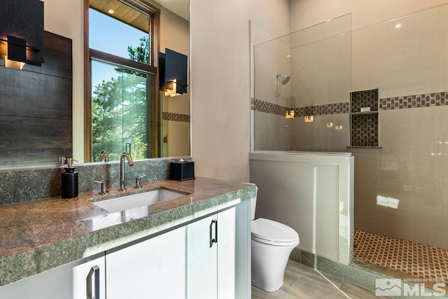 bathroom with tile patterned flooring, vanity, tiled shower, and toilet