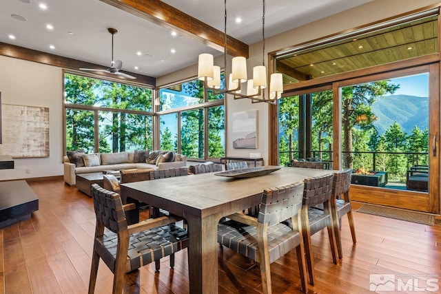 dining room with ceiling fan with notable chandelier, a healthy amount of sunlight, a mountain view, and hardwood / wood-style floors