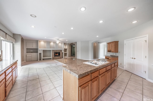 kitchen featuring light tile patterned flooring, a kitchen island, built in features, and white gas stovetop