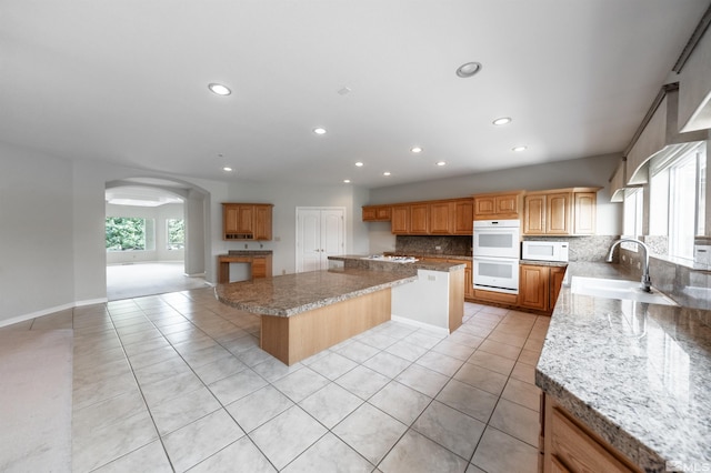 kitchen featuring white appliances, a kitchen island, decorative backsplash, light carpet, and sink