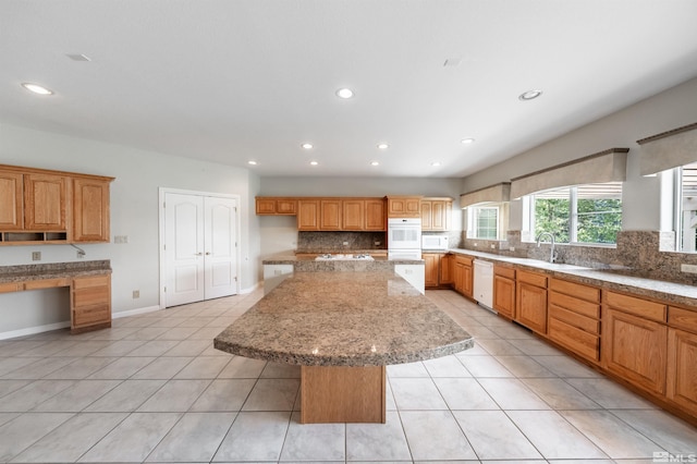 kitchen with built in desk, light tile patterned floors, a kitchen island, white appliances, and backsplash
