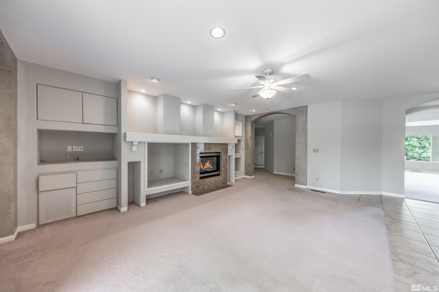 unfurnished living room with ceiling fan, light carpet, a high end fireplace, and built in shelves