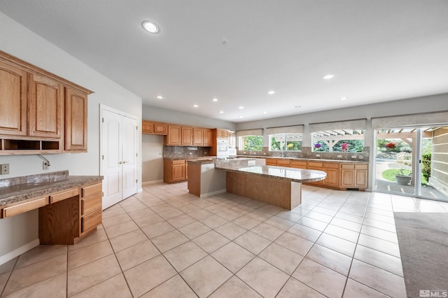 kitchen featuring light stone counters, backsplash, light tile patterned floors, and a center island