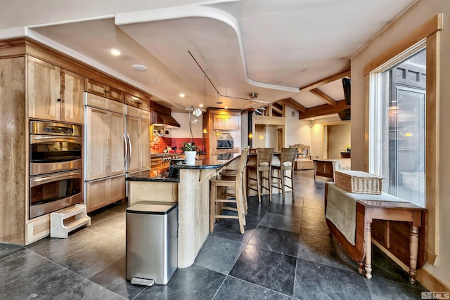 kitchen with dark tile patterned floors, wall chimney exhaust hood, stainless steel double oven, paneled built in refrigerator, and a center island