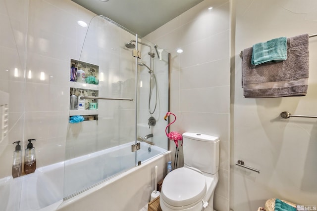 bathroom featuring tile walls, toilet, and shower / bath combination with glass door