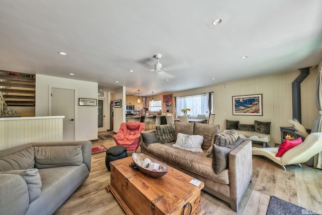 living room with a wood stove, light wood-type flooring, and ceiling fan