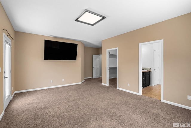 unfurnished bedroom with light carpet, a walk in closet, and ensuite bathroom