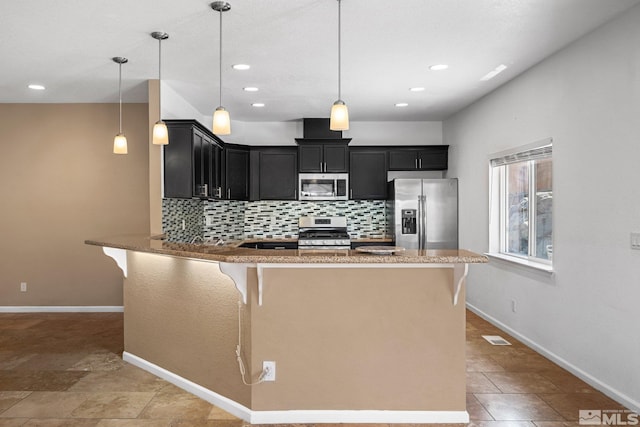 kitchen with decorative light fixtures, appliances with stainless steel finishes, a kitchen breakfast bar, kitchen peninsula, and backsplash