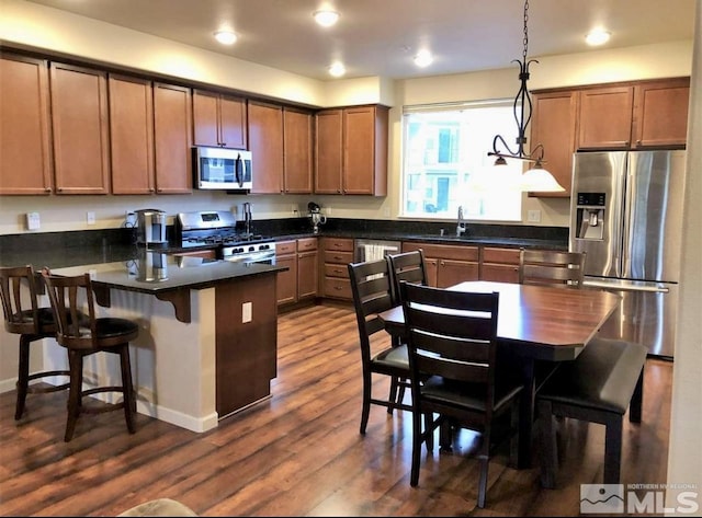 kitchen featuring appliances with stainless steel finishes, a breakfast bar, decorative light fixtures, sink, and dark hardwood / wood-style flooring