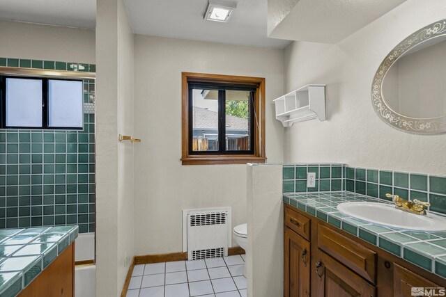 full bathroom featuring combined bath / shower with glass door, radiator heating unit, tile patterned flooring, toilet, and vanity