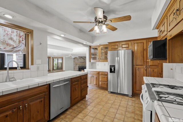 kitchen with a fireplace, decorative backsplash, stainless steel appliances, and tile countertops