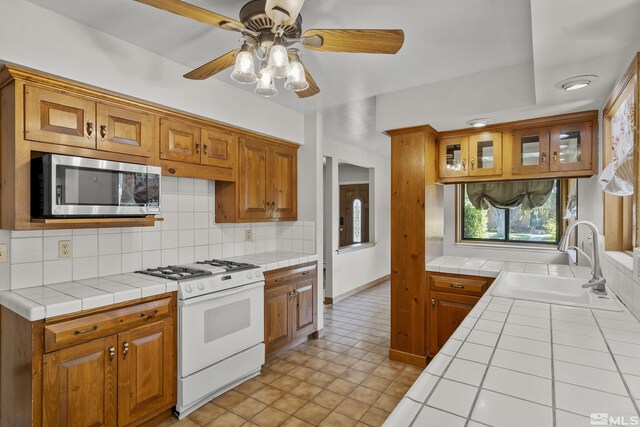 kitchen featuring sink, white gas range oven, tile countertops, and ceiling fan