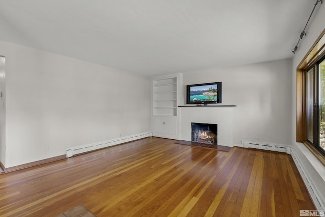 unfurnished living room featuring a brick fireplace, built in shelves, wood-type flooring, and baseboard heating