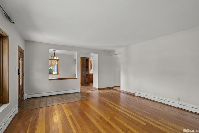 spare room featuring wood-type flooring, a baseboard heating unit, and a notable chandelier