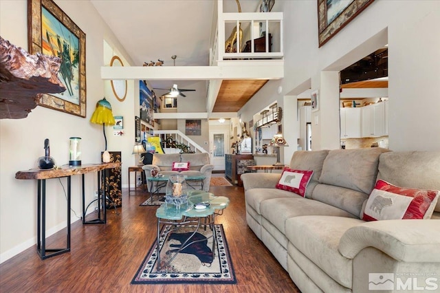 living room featuring dark wood-type flooring, ceiling fan, and a towering ceiling