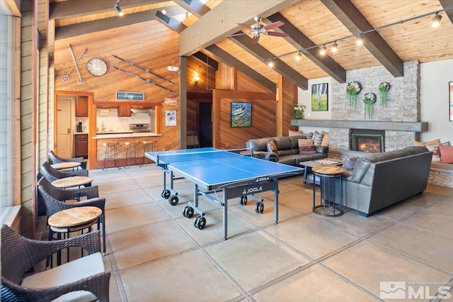 game room with wood ceiling, wooden walls, high vaulted ceiling, a stone fireplace, and beamed ceiling