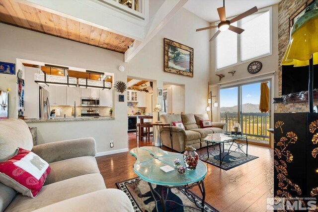 living room with a towering ceiling, beamed ceiling, dark hardwood / wood-style flooring, ceiling fan, and wood ceiling