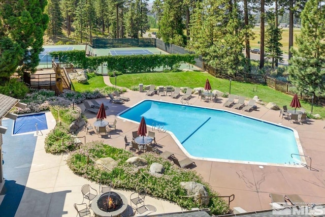 view of pool featuring an outdoor fire pit, tennis court, a patio, and a lawn