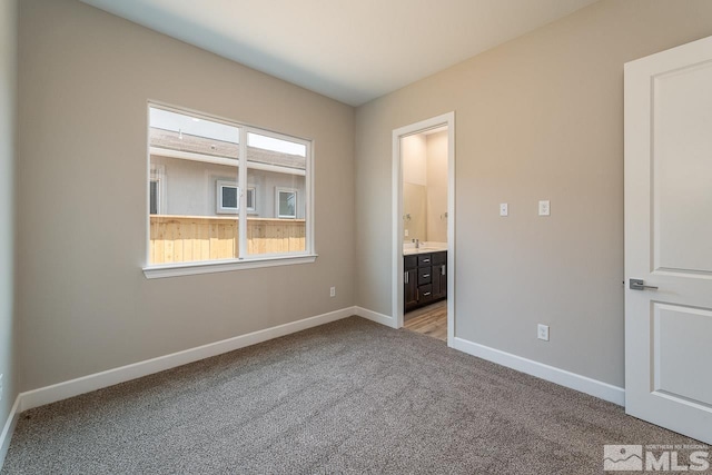 unfurnished bedroom featuring sink, light colored carpet, and ensuite bathroom